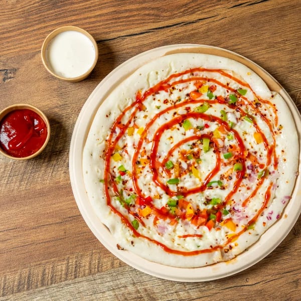 Savory uttapam topped with colorful vegetables, cheese, and a swirl of red sauce, served with two dipping sauces.