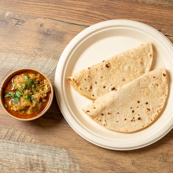 Two folded flatbreads on a white plate next to a bowl of chicken curry with cilantro.