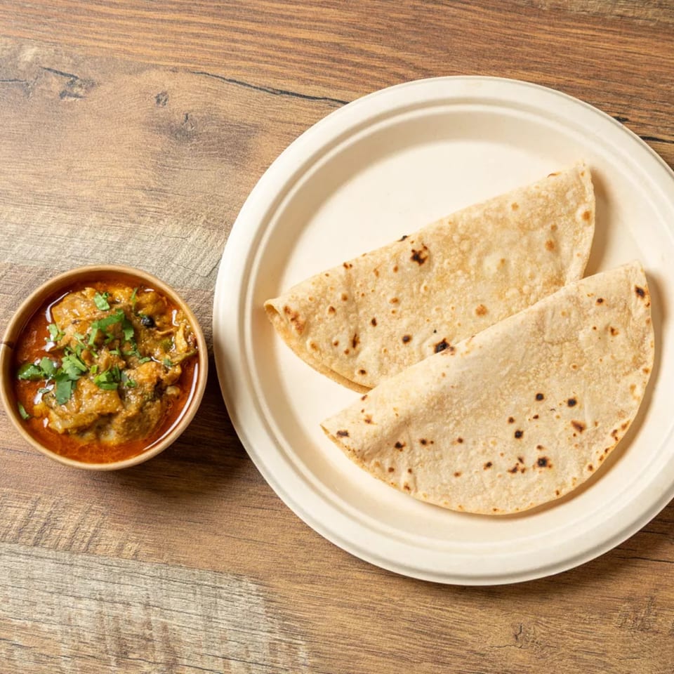Two folded flatbreads on a white plate next to a bowl of chicken curry with cilantro.