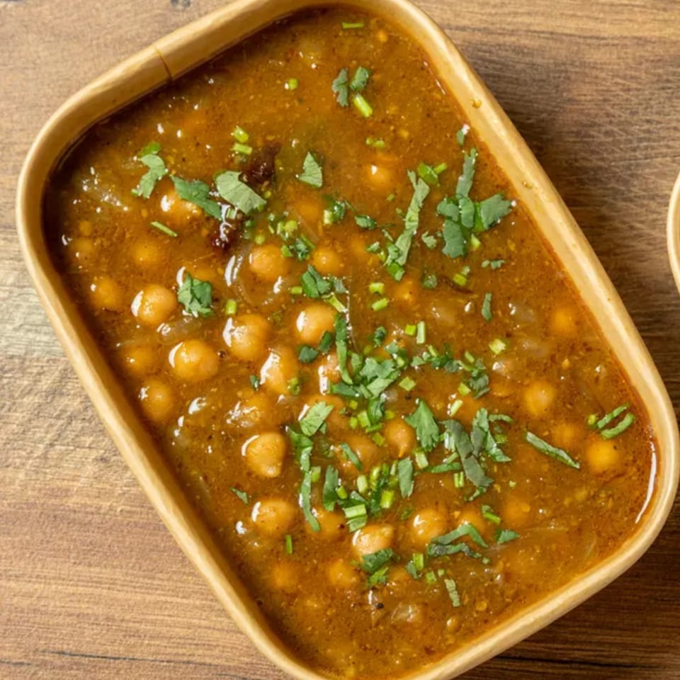 A rectangular bowl of chana masala, a chickpea curry, garnished with fresh cilantro.