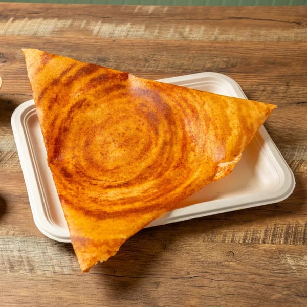 A triangular dosa with a spiral pattern, served on a white rectangular plate on a wooden table.