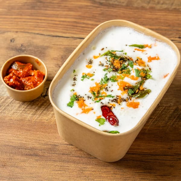 Creamy yogurt dish with spices, herbs, and a red chili, next to a small cup of red pickle.